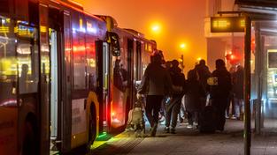 Fahrgäste stehen abends an einer Bushaltestelle und steigen in den Bus ein. (Foto: picture alliance / Jochen Tack)