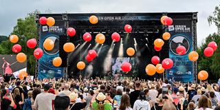 Orangene und rote Luftballons fliegen über dem Publikum. Im Hintergrund ist eine Bühne zu sehen. (Foto: Dirk Guldner)