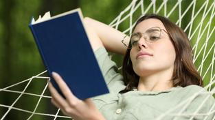 Eine Frau liegt in einer Hängematte und liest ein Buch (Foto: IMAGO / Panthermedia / PheelingsMedia)
