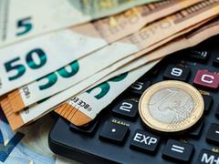 Geldscheine und eine Münze liegen auf einem Taschenrechner (Foto: IMAGO / Zoonar)