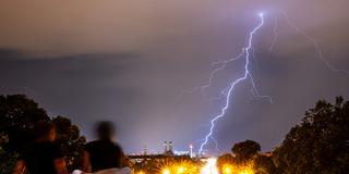 Zwei Personen beobachten bei Gewitter einen Blitz am Himmel über der Stadt (Foto: picture alliance/dpa | Peter Kneffel)